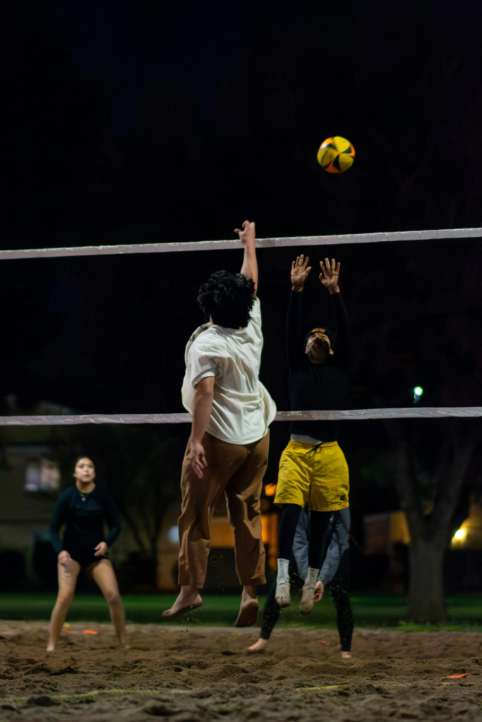 Players jumping to hit a volleyball during a nighttime beach game