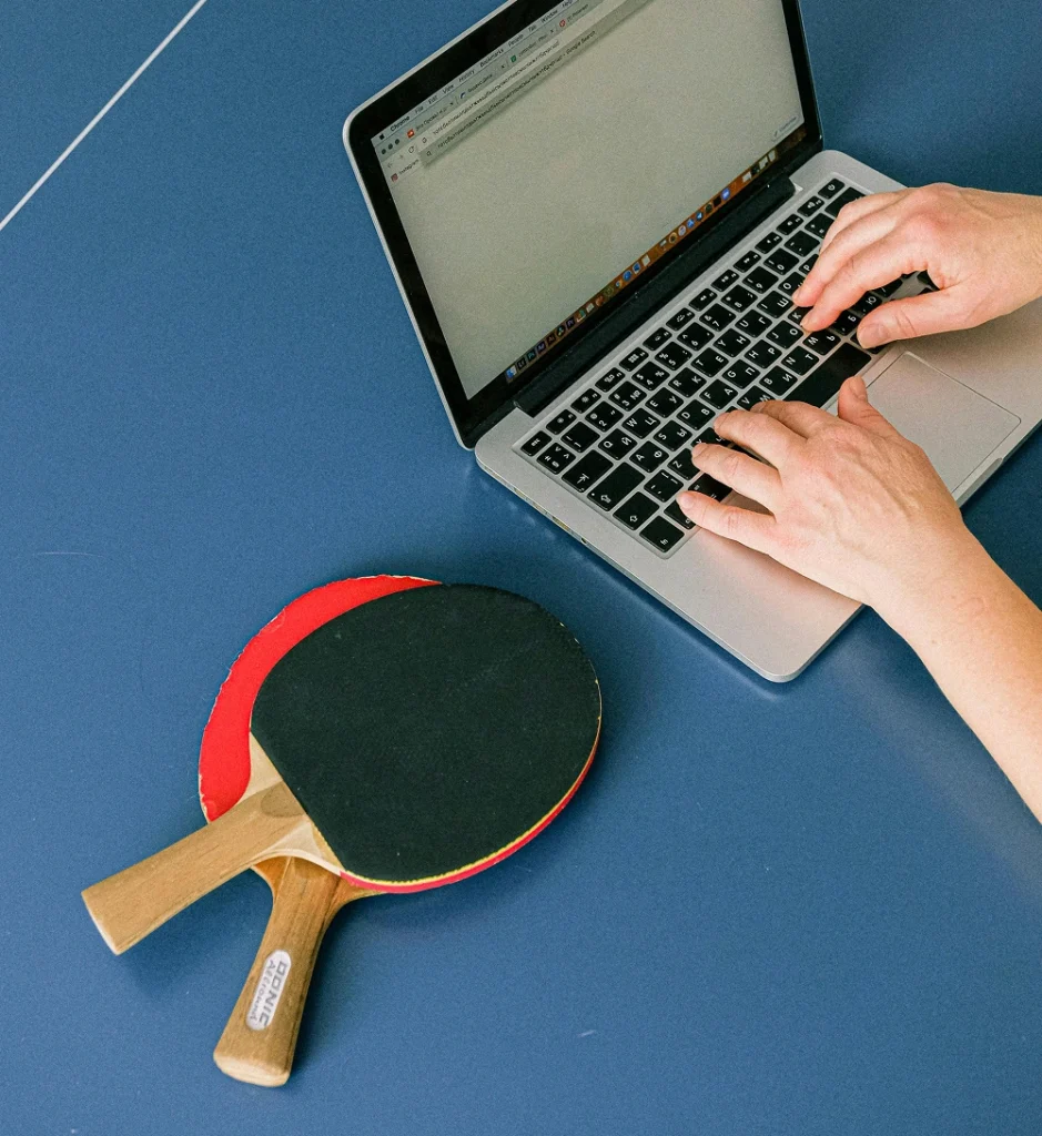 Person using a laptop next to table tennis paddles on a table