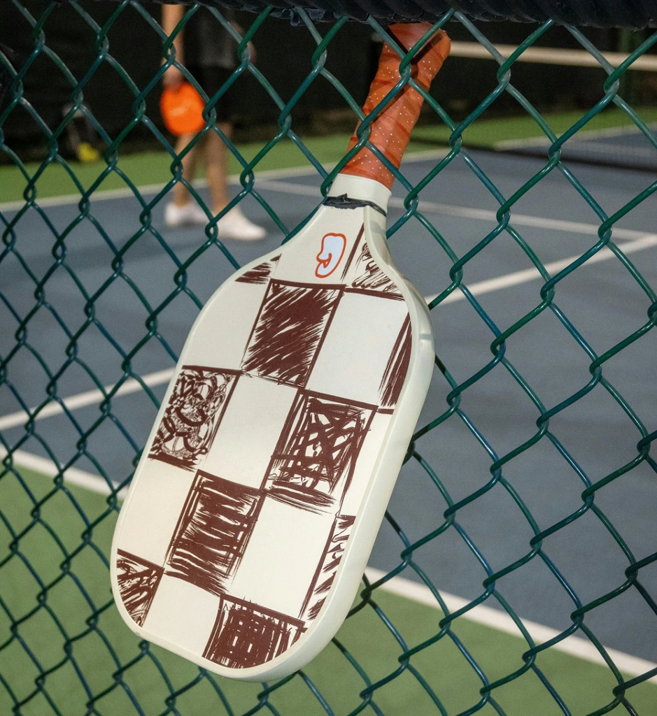 Padel racket hanging on a fence beside an outdoor court