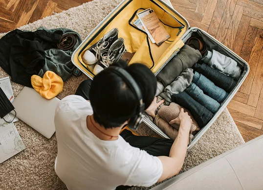 Person packing clothes into an open suitcase at home